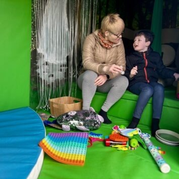 a lady engages with a young boy surrounded by sensory toys on the padded mats