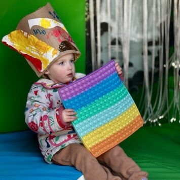 a child wearing a crafted headpiece engages with a large rainbow pop-it