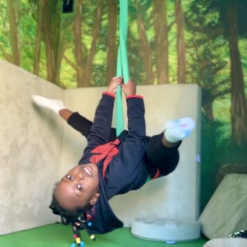 A young acrobatic girl hangs upside down on the sensory swing
